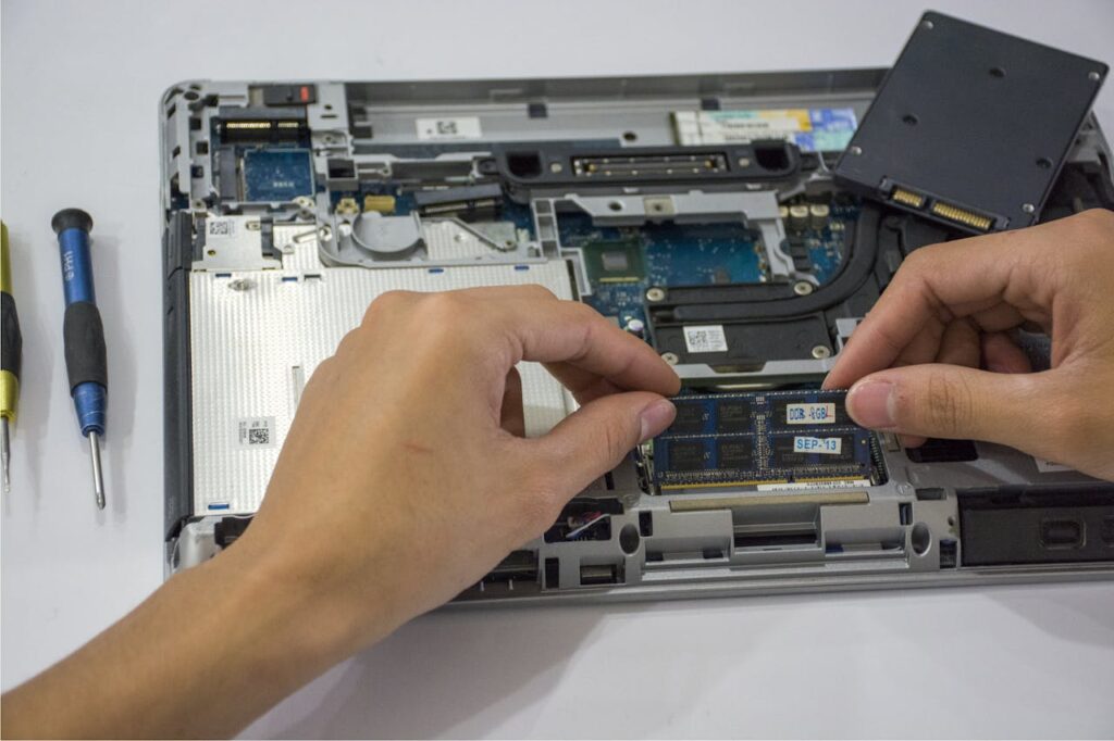 Close-up of a technician assembling a laptop's internal components using tools.